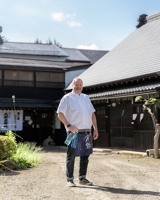 Stuart Morris standing and holding bottles of sake in from of Shindo Brewery